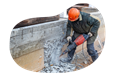 A demolition contractor works on a foundation with a jackhammer.