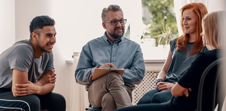 A group of three people sitting with a therapist in a bright office.