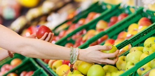 A hand looking through produce at a market.