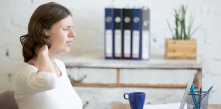 A woman rubbing her neck in pain at work.