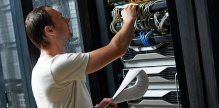 An IT technician completes a checklist in a server room.