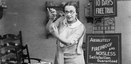 Woman displays a set of false teeth in vintage setting.