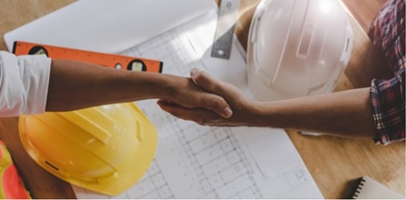 Two construction contractors shake hands over building plan.