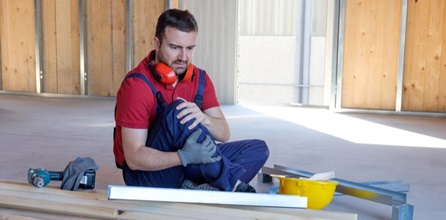 A construction worker clutching his knee in pain.