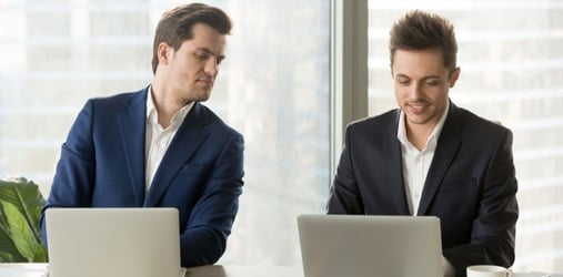 A man glancing at another man's laptop screen.