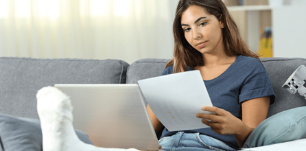 Woman in a leg cast with a laptop reviewing paperwork.