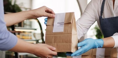 Employee handing a customer a bag using safety gloves.