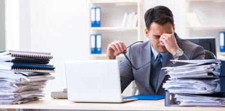 Overworked business person at desk with paperwork.