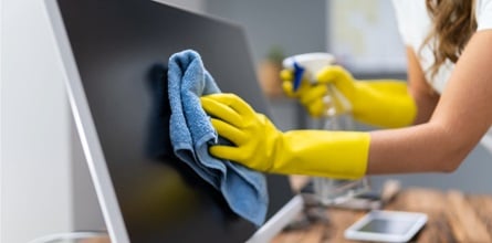 Cleaning employees spraying and wiping down an office desk and computer.