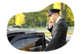 A chauffeur talks on the phone while getting into their limo.