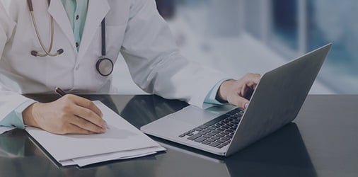 Medical professional working with a laptop and a stack of papers.